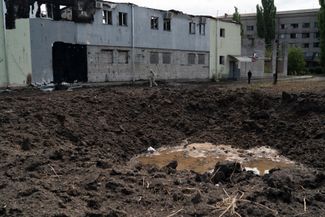 Люди проходят мимо воронки от взрыва в Славянске. Снаряд упал рядом со зданием, где размещается украинский Красный Крест. Город находится под контролем Украины