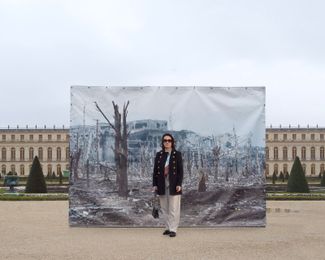 Forty-year-old makeup artist Yuliia stands in front of a photograph of the destroyed Donetsk Airport, taken by Vasily Maximov. Versailles, France.