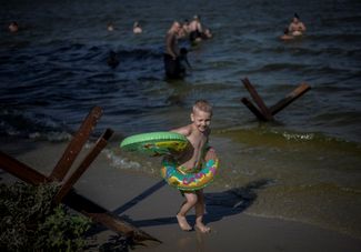 Мальчик рядом с противотанковыми ежами на берегу Днепра в Запорожье, где 6 августа температура достигла отметки 40 градусов
