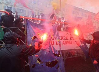 Протестующие сжигают флаги ЕС и НАТО во время демонстрации, один из слоганов которой «Больше никакого оружия, давайте остановим войну в Украине».