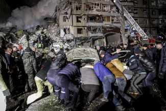 Местные жители помогают спасателям оттащить поврежденную обломками машину от дома в Днепре, в который попала российская ракета