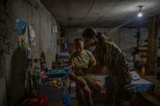 Украинский военный медик меряет давление немолодому солдату в расположении части на Харьковском фронте