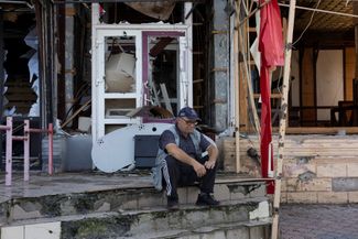 Житель Изюма, недавно освобожденного украинскими вооруженными силами, сидит перед разрушенным зданием