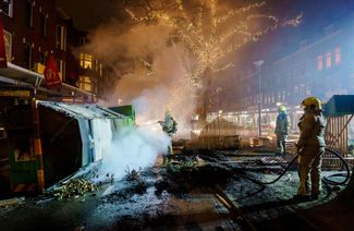 Пожарные тушат огонь, вспыхнувший на одной из улиц Роттердама во время беспорядков, 25 января 2021 года