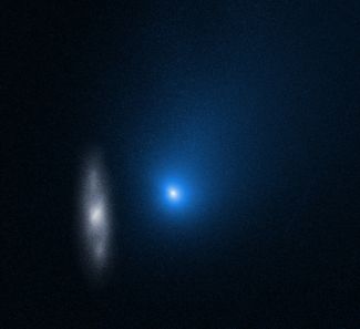Комета на фоне далекой спиральной галактики 2MASX J10500165-0152029. Яркое центральное ядро последней размазано по изображению, потому что «Хаббл» следил за кометой. Снимок от 16 ноября 2019