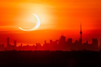 Частное кольцевое солнечное затмение поднимается над Торонто 10 июня 2021 года. Кольцевое затмение возникает в тот момент, когда Луна, находящаяся на дальнем участке своей немного вытянутой орбиты, перекрывает солнце. Видимый размер Луны в этот момент меньше солнечного диска, поэтому внешний край солнца продолжает освещать Землю.