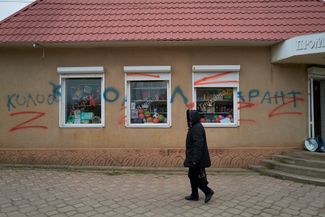 Жительница Снигиревки в Николаевской области проходит мимо здания продуктового магазина. На стене видны надпись «коллаборант» и литеры Z, ставшие символом путинской агрессии