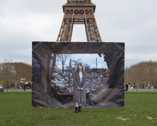 Anna, a 30-year-old real estate manager, stands in front of a photograph of ruins in Chernihiv, taken by Mykhaylo Palinchak. Paris, France.