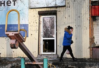Жительница Донецка идет мимо здания, на стенах которого остались следы от осколков