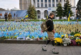 Боец ВСУ с протезами ног идет мимо мемориала на площади Независимости в Киеве. Каждый флаг поставлен в память о погибшем военнослужащем