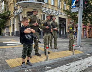 Мальчик с игрушечным оружием стоит рядом с украинскими военными, патрулирующими район в центре Киева. Украинские СМИ последние несколько дней активно обсуждают возможность нового наступления российских войск на Киев