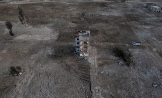Вид с воздуха на расчищенный от руин жилой участок: до землетрясения здесь было множество зданий, сейчас — только один поврежденный дом. Снимок сделан в турецкой области Хатай на границе с Сирией. Все фотографии в этом материале сделаны в начале февраля 2024 года