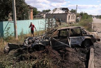 Житель Славянска идет мимо автомобиля, сгоревшего в результате авиаудара