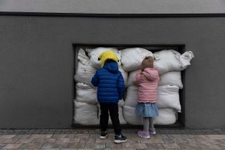 Дети смотрят на мешки с песком, которые закрывают окна в детском саду. Львов