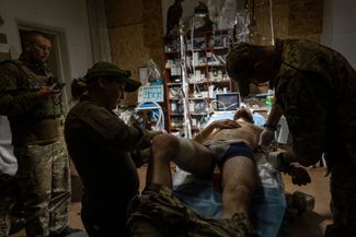 Военные врачи помогают раненому украинскому солдату в полевом госпитале под Бахмутом, где продолжаются тяжелые бои, начавшиеся почти год назад