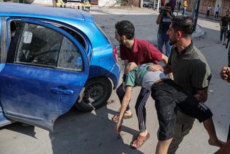 Раненого жителя сектора Газа грузят в автомобиль, чтобы доставить в больницу. Он пострадал в результате израильского авиаудара 2 ноября 2023 года