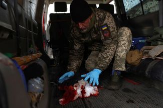Украинский военный медработник стирает кровь с пола машины после того, как доставил раненого в госпиталь