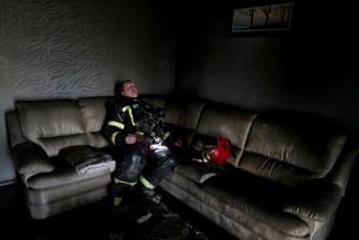 Пожарный отдыхает после тушения огня. Пожар в жилом доме возник из-за военных действий.