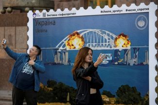 Киевляне делают селфи на фоне плаката, изображающего почтовую марку со взрывом на Крымском мосту. 8 октября «Укрпочта» официально объявила о выпуске такой марки