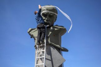 Активист символически обматывает бинтами пострадавший от обстрела памятник украинскому писателю Тарасу Шевченко в городе Бородянка к северо-западу от Киева
