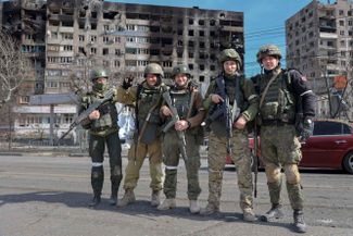 Военнослужащие Донецкой Народной Республики фотографируются на улице перед жилыми домами, пострадавшими после обстрелов и боев на окраине Мариуполя