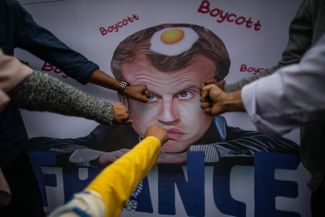 Протестующие бьют плакат с карикатурой на президента Франции Эмманюэля Макрона в Джакарте, Индонезия. 2 ноября 2020 года