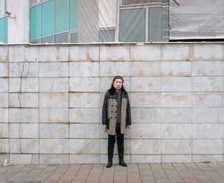 Ainur in front of a marble wall where shots from a heavy machine gun are still visible. Almaty, 2022.