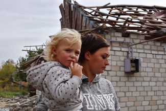 Жительница села Беленькое вместе с дочерью стоит возле одного из домов, пострадавших при обстреле