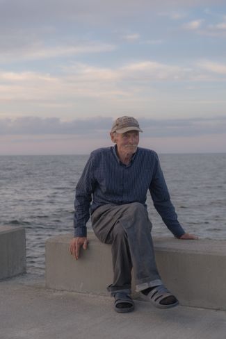 Anton, a fisherman, sits on the pier in Pāvilosta. July 2024.