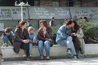 Residents of Sarajevo basking in the sun during a three-week truce. The wall behind them shows graffiti cursing the UN. 1994.