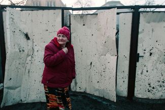 Жительница Харькова у поврежденного осколками снарядов забора