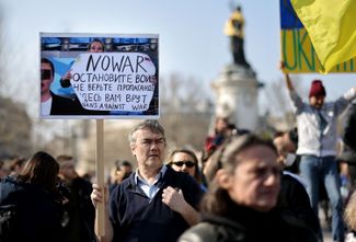 A protester in Paris carries a sign with a screenshot of Ovsyannikova’s TV protest. March 19, 2022.