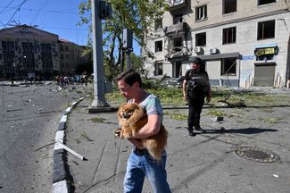 Житель Харькова с собакой на руках на фоне зданий, частично разрушенных падением российских авиабомб