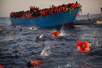Мигранты, по большей части из Эритреи, прыгают из переполненной лодки в 13 милях от побережья Ливии, 29 августа<br><br>