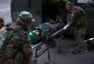 Украинские врачи перевозят раненого военнослужащего, доставленного с фронта. Пострадавшему оказывают помощь в полевом госпитале ВСУ, развернутом на контролируемой Киевом территории Донецкой области