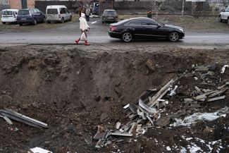 Жительница поселка Глеваха Киевской области идет мимо воронки, оставшейся после ракетного удара. Глеваха находится в 25 километрах к юго-западу от Киева