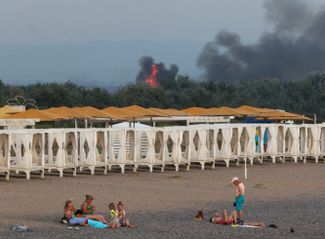 Отдыхающие на пляже в Новофедоровке на фоне дыма над российской военной авиабазой