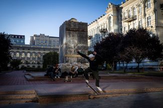 Подросток катается на скейтборде на фоне укрытого от обстрелов памятника украинскому композитору Николаю Лысенко на Театральной площади рядом с Национальной оперой