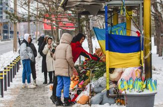 Жители Днепра несут цветы, флаги, свечи и мягкие игрушки к автобусной остановке у разрушенной многоэтажки на набережной Победы