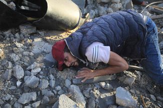 Мужчина прослушивает руины разрушенного израильскими военными здания в поисках людей, находящихся под завалами. Центральная часть сектора Газа, 6 ноября 2023 года