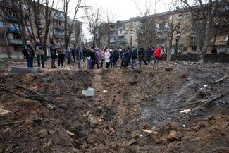 Жители Киева возле воронки, которая образовалась после попадания в землю российской ракеты во время массированного ракетного обстрела города в новогоднюю ночь​