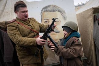 Член исторического клуба в форме времен Второй мировой войны показывает оружие мальчику возле портрета Иосифа Сталина на военно-исторической выставке на Дворцовой площади в Санкт-Петербурге. Экспозиция приурочена к 80-летию со дня снятия блокады Ленинграда (27 января 1944 года)