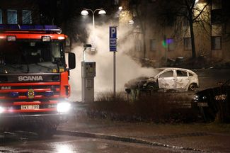 Пожарные тушат автомобиль, подожженный во время беспорядков в Ринкебю. Февраль 2017 года