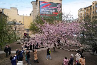 Жители Санкт-Петербурга в Саду Дружбы. На билборде — реклама военной службы по контракту с лозунгом «Служить России — это настоящая работа»