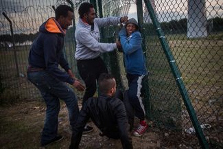 Мигранты пролезают в дыру в заборе рядом с терминалом Евротоннеля в Кале