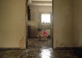 Жительница Херсона убирает грязь с пола в квартире, из которой только ушла вода