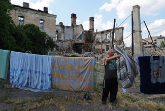 Житель Лисичанска развешивает белье на фоне развалин жилого дома