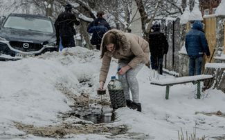 Жительница Харькова вычерпывает смесь воды и топлива, растекшуюся по улице