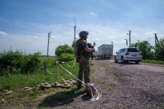 Украинский солдат стоит на позиции, пока грузовики с погибшими россиянами едут к границе