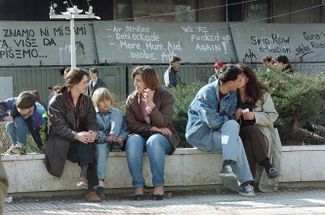 Residents of Sarajevo basking in the sun during a three-week truce. The wall behind them shows graffiti cursing the UN. 1994.
